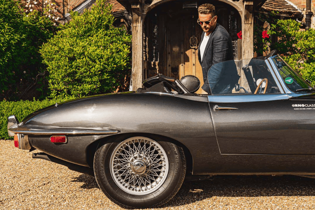 A man getting into a Jaguar E-Type sportscar branded with the RNG Classics logo