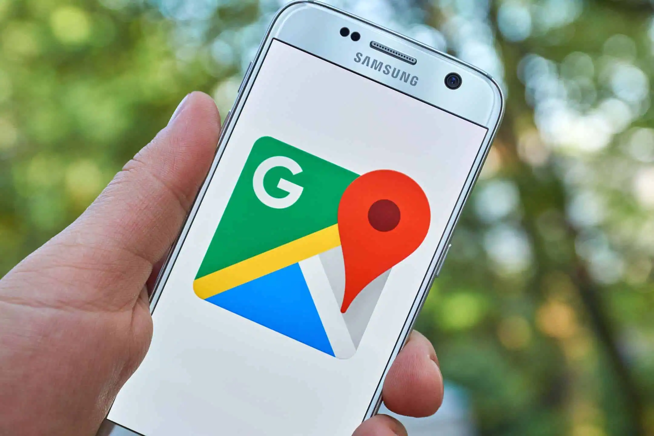 A hand holding a smartphone displaying the Google Maps logo