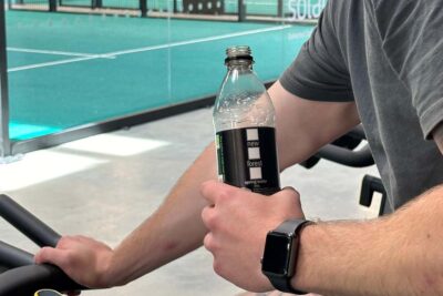 A person working out at a gym holding a bottle of New Forest Water