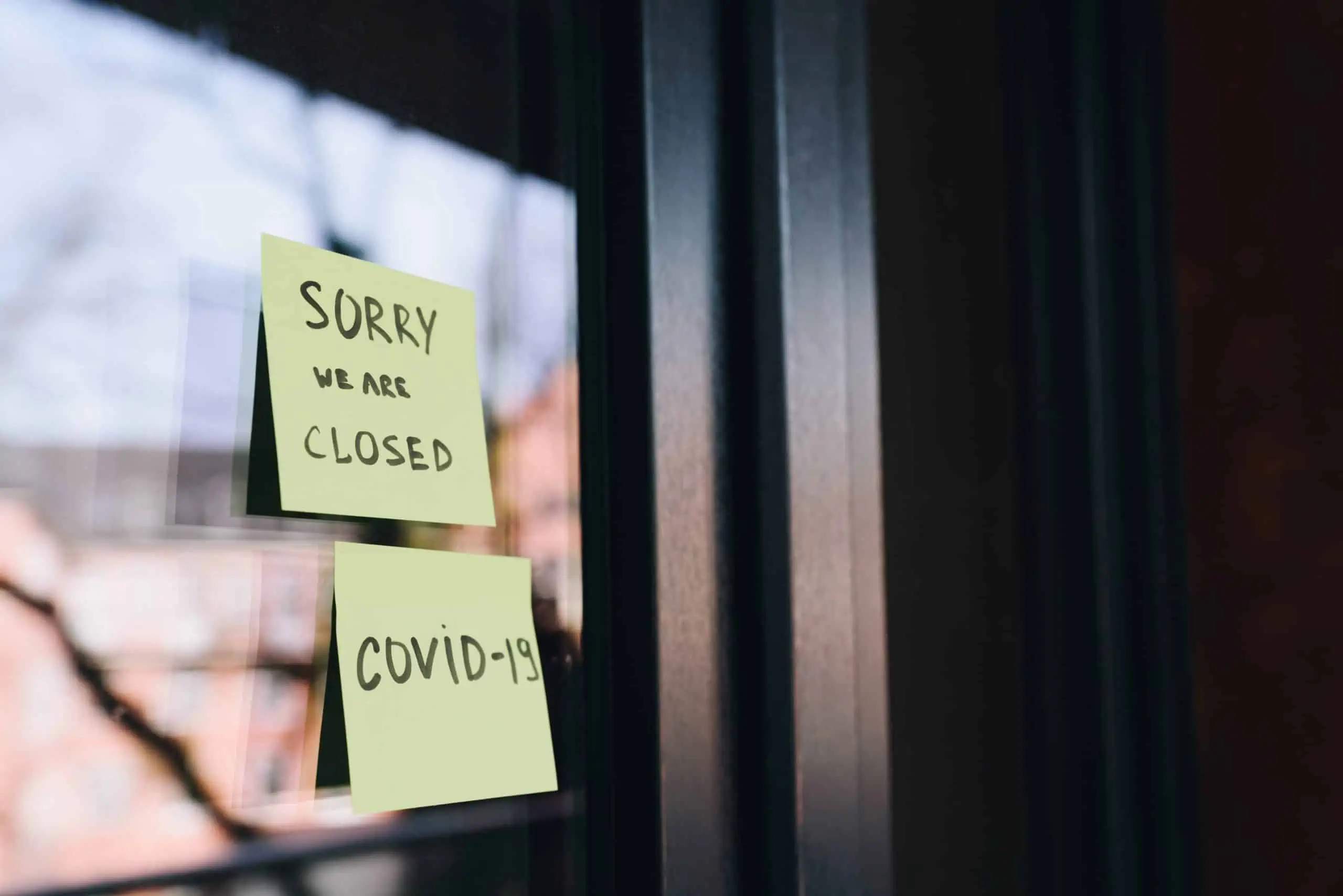 A door with two Post-it notes stuck to it, reading Sorry we're closed, COVID-19