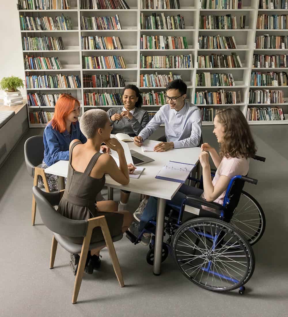 A group of young adults around a desk at a library, one of whom is in a wheelchair